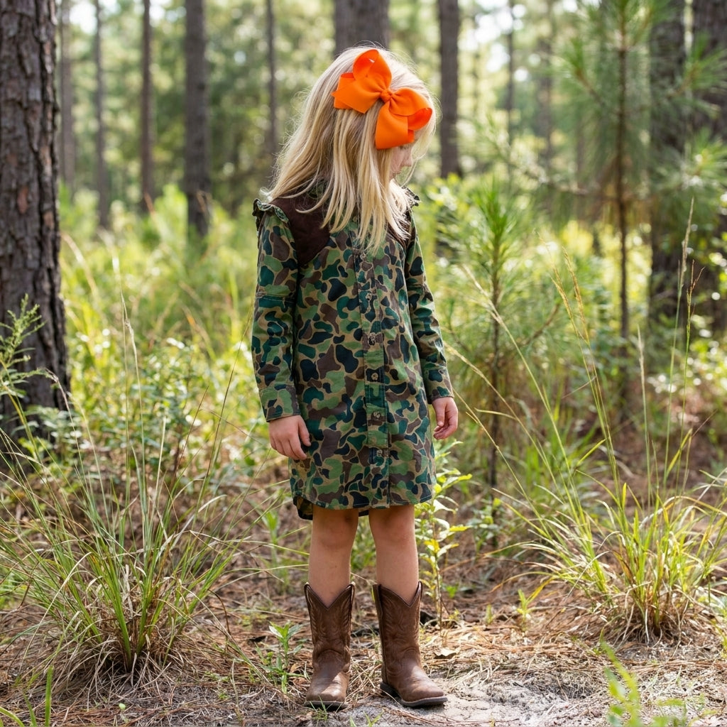 Girl wearing a vintage camo cotton-blend shirt dress with brown recoil pads and brown cowboy boots in a forest.
