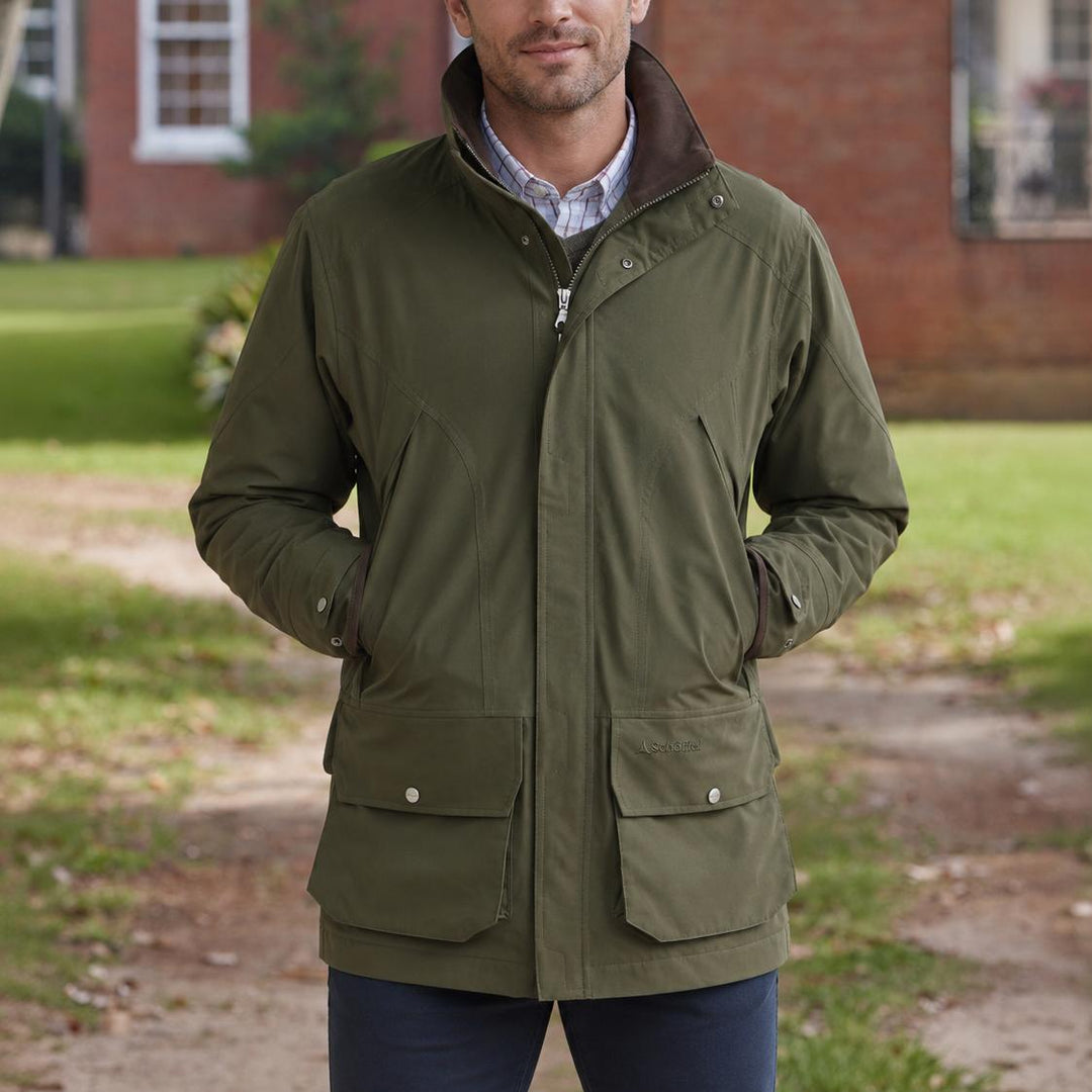 Olive green Schoffel Snipe ultralight shooting coat with large cartridge pockets and a brown collar in a field setting.