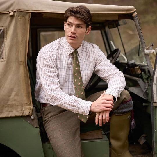 Man wearing a Schoffel Burnham tattersall check cotton shirt with a green patterned tie, seated in a vintage off-road vehicle.