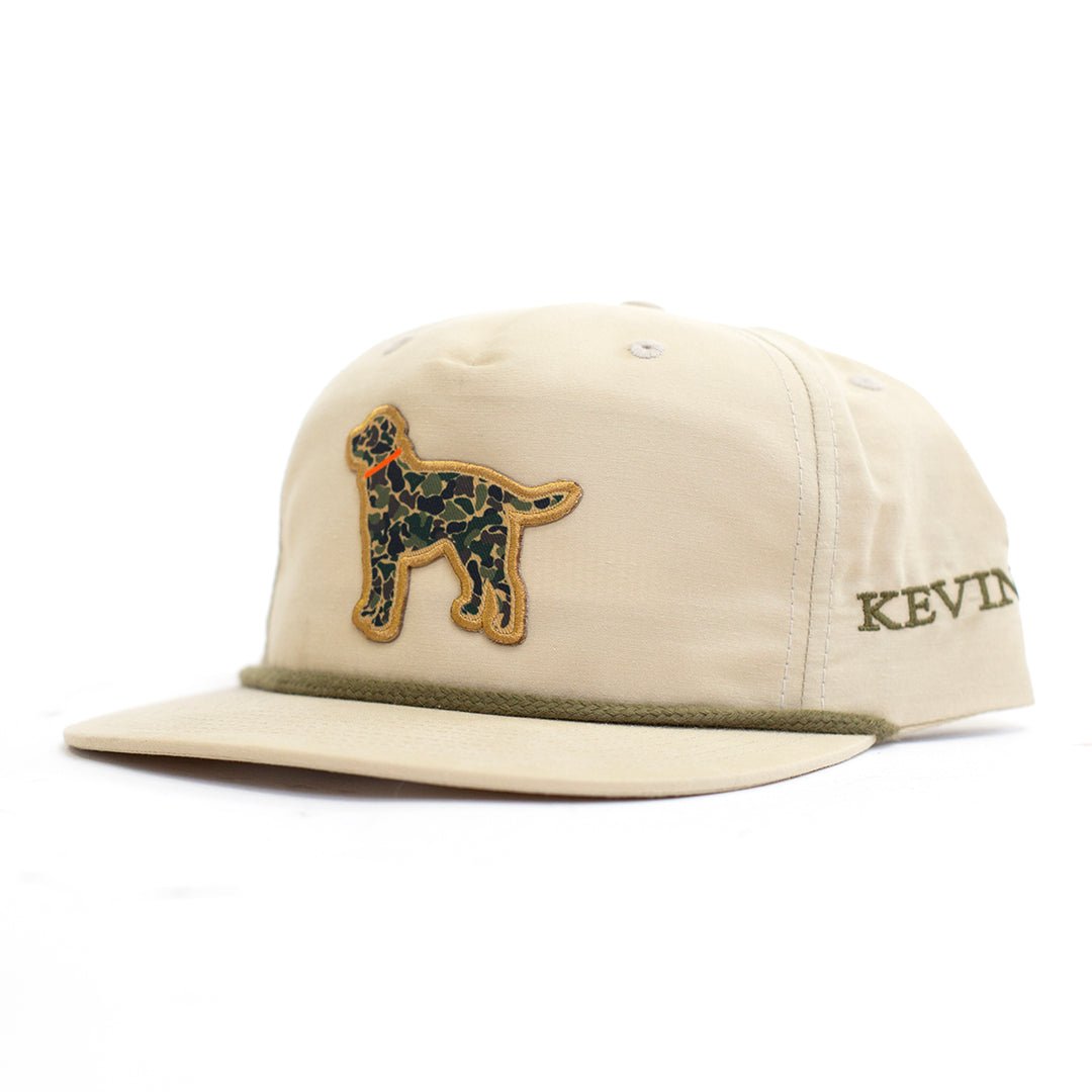 A beige 5-panel baseball cap with a green camouflage dog patch on the front and 'KEVIN'S' embroidered on the side, set against a plain white background.