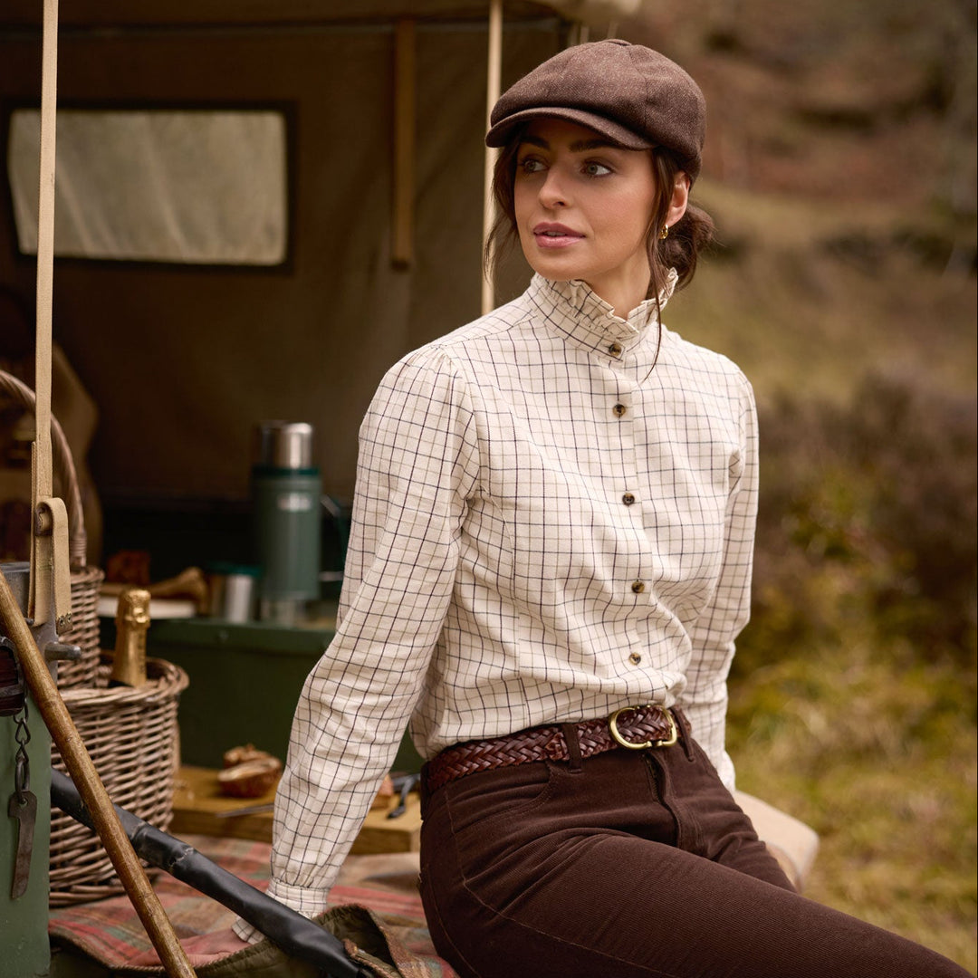 Woman wearing a cream check brushed cotton Sheringham shirt with a pie-crust collar and brown trousers outdoors.