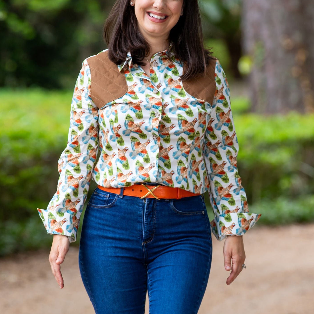 Woman wearing a white long-sleeve shooting shirt with a quail print and brown suede shoulder patches, paired with blue jeans.