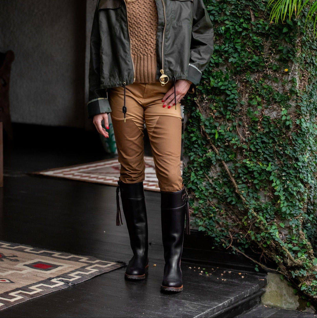 Woman wearing tan high-rise stretch briar pants with reinforced front panels, styled with a brown sweater and tall black boots.