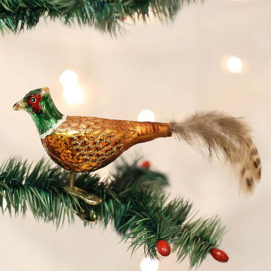 Hand-painted blown glass pheasant ornament with glittered gold body, green head, and real feather tail on a pine branch.