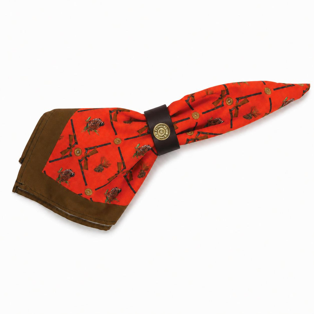 Brown leather napkin ring featuring a brass shotshell concho, holding a red hunting-themed napkin with shotgun and pinecone print.