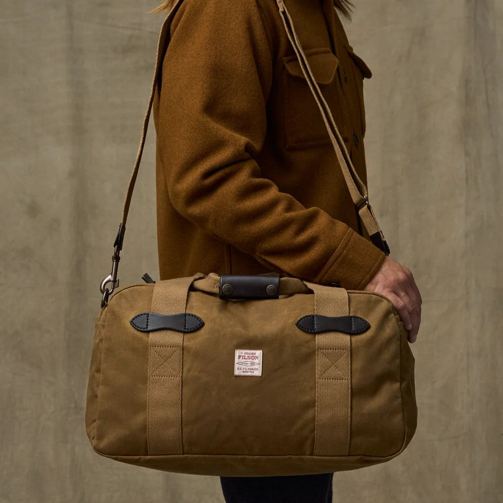 Tan Filson Tin Cloth small duffle bag with Bridle Leather accents and cotton webbing straps being carried over a shoulder.