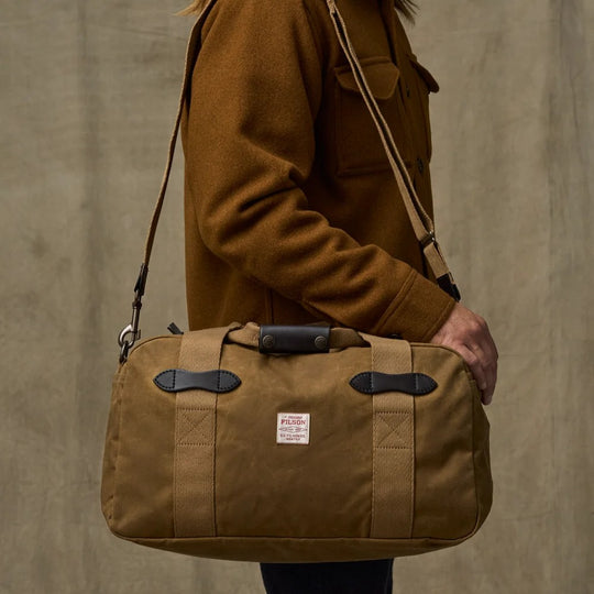 Tan Filson Tin Cloth small duffle bag with Bridle Leather accents and cotton webbing straps being carried over a shoulder.