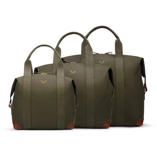 Three olive green Bennett Winch cargo bags in small, medium, and large sizes with brown leather trim and brass hardware.
