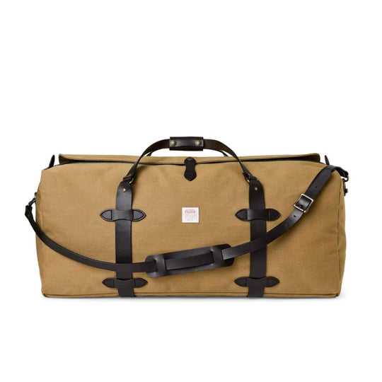 Tan Filson large duffle bag in rugged twill with dark brown bridle leather straps, handles, and a shoulder strap.