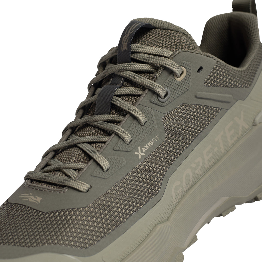 A close-up of a gray and olive green hiking shoe with textured mesh and synthetic overlays, featuring 'X-AXISFIT' and 'GORE-TEX' branding on the side.