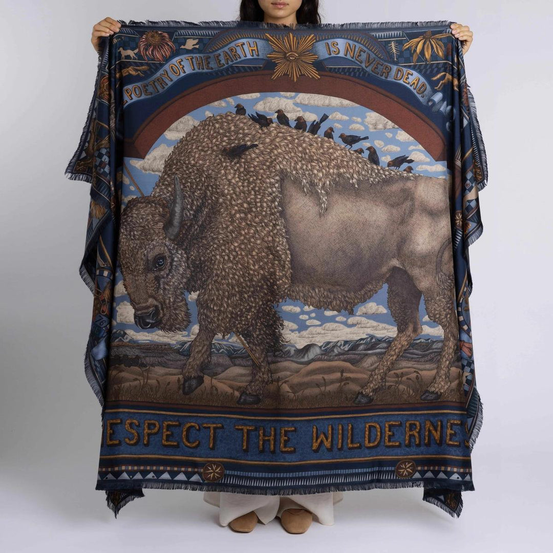 Sabina Savage silk rectangle scarf featuring a detailed bison illustration, folk art motifs, and blue borders with fringe.