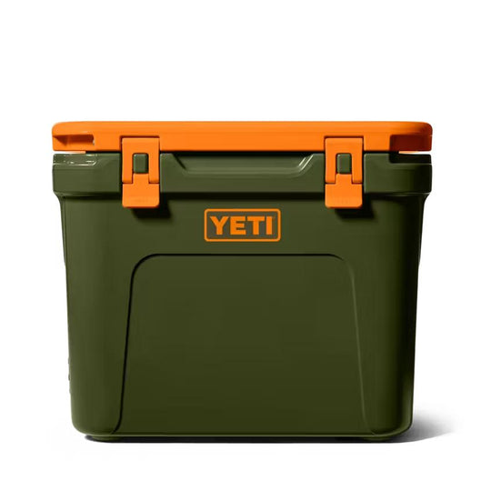 Olive green YETI Roadie 32 wheeled cooler with a bright orange lid and matching latch accents against a white background.