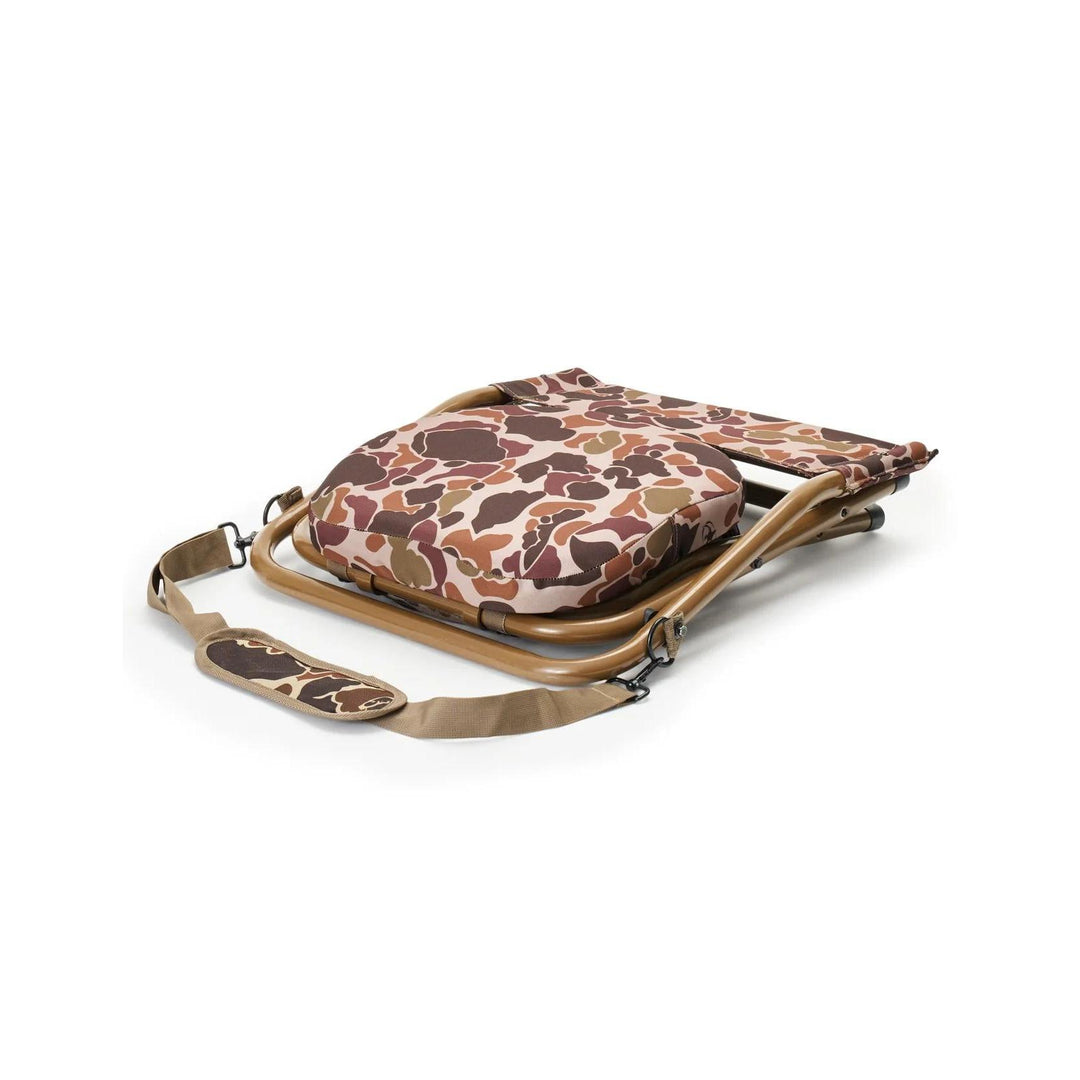 Rig 'Em Right Hyde Stool folded flat with a camo padded seat, brown metal frame, and adjustable shoulder strap.