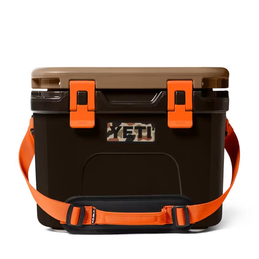 YETI Roadie 15 cooler in brown with orange latches, a camouflage logo, and a bright orange shoulder carrying strap.