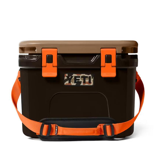 YETI Roadie 15 cooler in brown with orange latches, a camouflage logo, and a bright orange shoulder carrying strap.