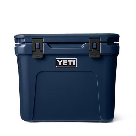 Navy blue YETI Roadie 32 wheeled cooler with a durable, compact design and black latch closures on a white background.